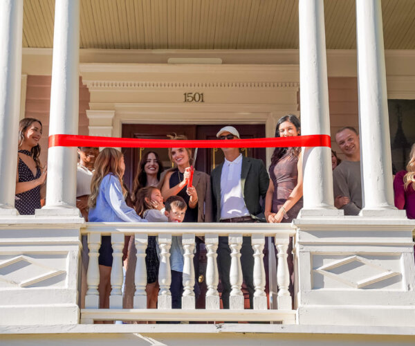 Picture of people standing on a balcony behind a red ribbon, about to cut the ribbon for the grand opening of Spa Ashton