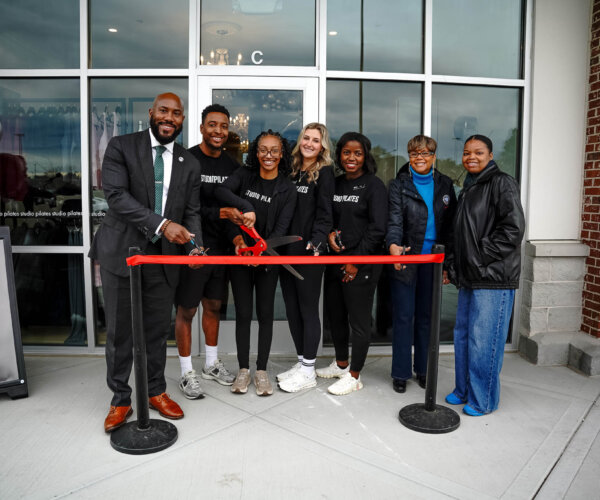 Picture of people standing behind a red ribbon, about to cut it for the grand opening of Studio Pilates