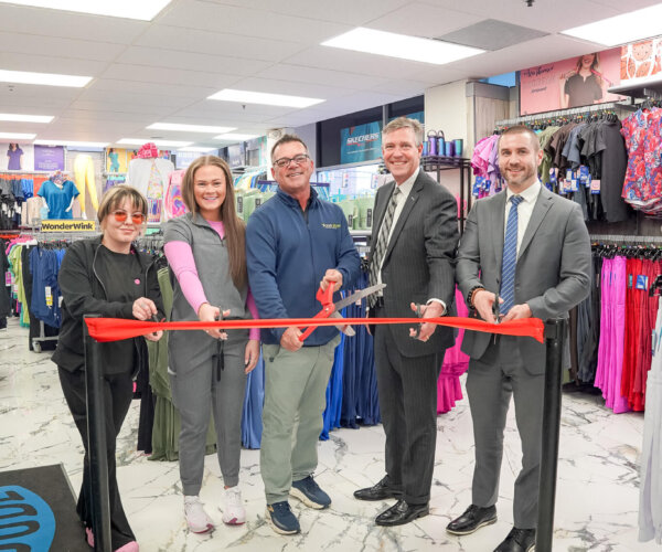 Picture of people standing behind a red ribbon, about to cut it for the grand opening of The Scrub Shop