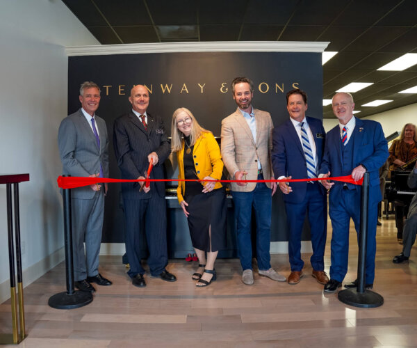 Picture of people standing behind a red ribbon, about to cut it for the grand opening of Steinway & Sons Piano Gallery