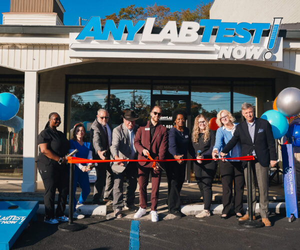 Picture of people standing behind a red ribbon, about to cut it for the grand opening of Any Lab Test Now!